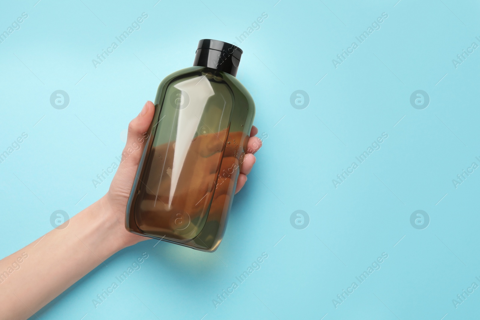 Photo of Woman holding shampoo bottle on turquoise background, top view. Space for text