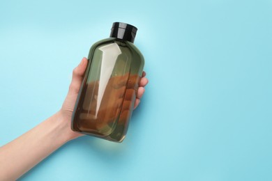 Woman holding shampoo bottle on turquoise background, top view. Space for text