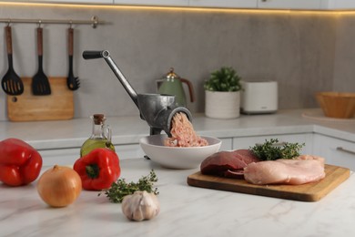 Photo of Metal meat grinder with chicken mince and products on white marble table in kitchen