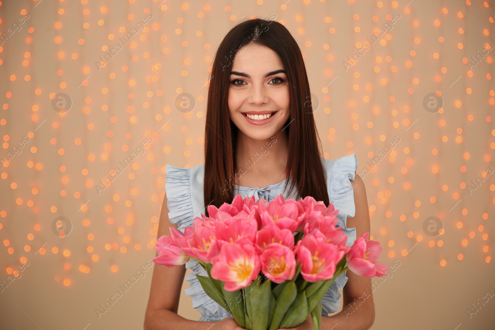 Photo of Portrait of smiling young girl with beautiful tulips on blurred background. International Women's Day