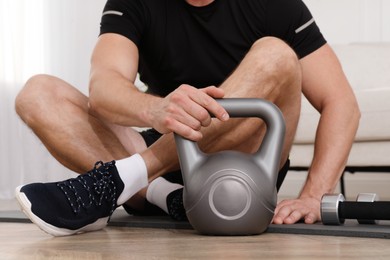 Photo of Muscular man sitting with kettlebell on mat at home, closeup
