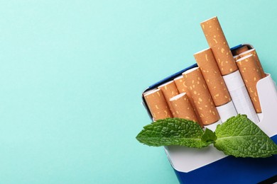 Photo of Pack of menthol cigarettes and mint on turquoise background, top view. Space for text