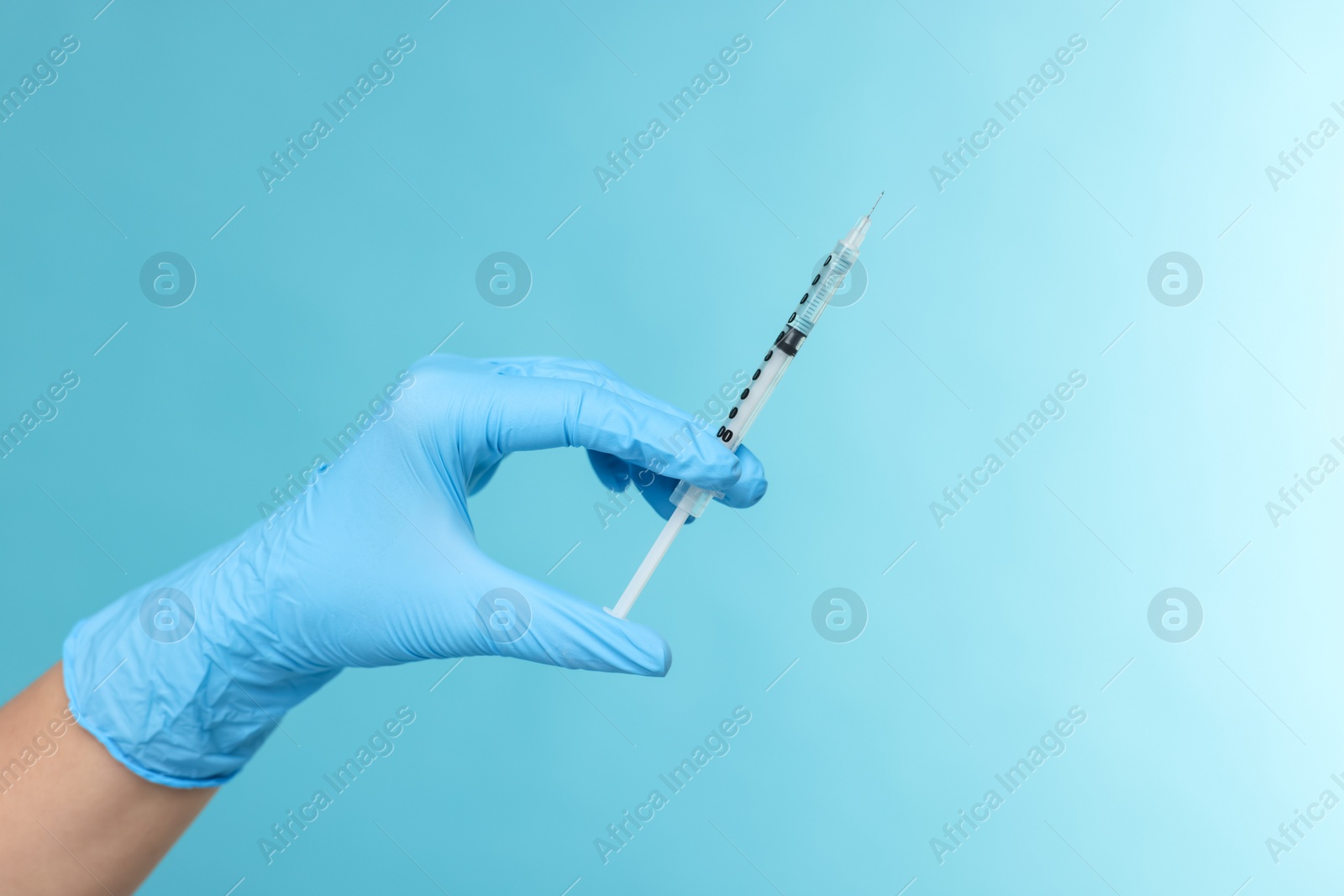 Photo of Doctor holding syringe on light blue background, closeup