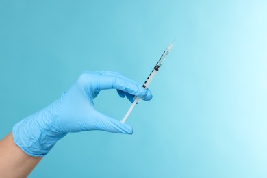 Doctor holding syringe on light blue background, closeup