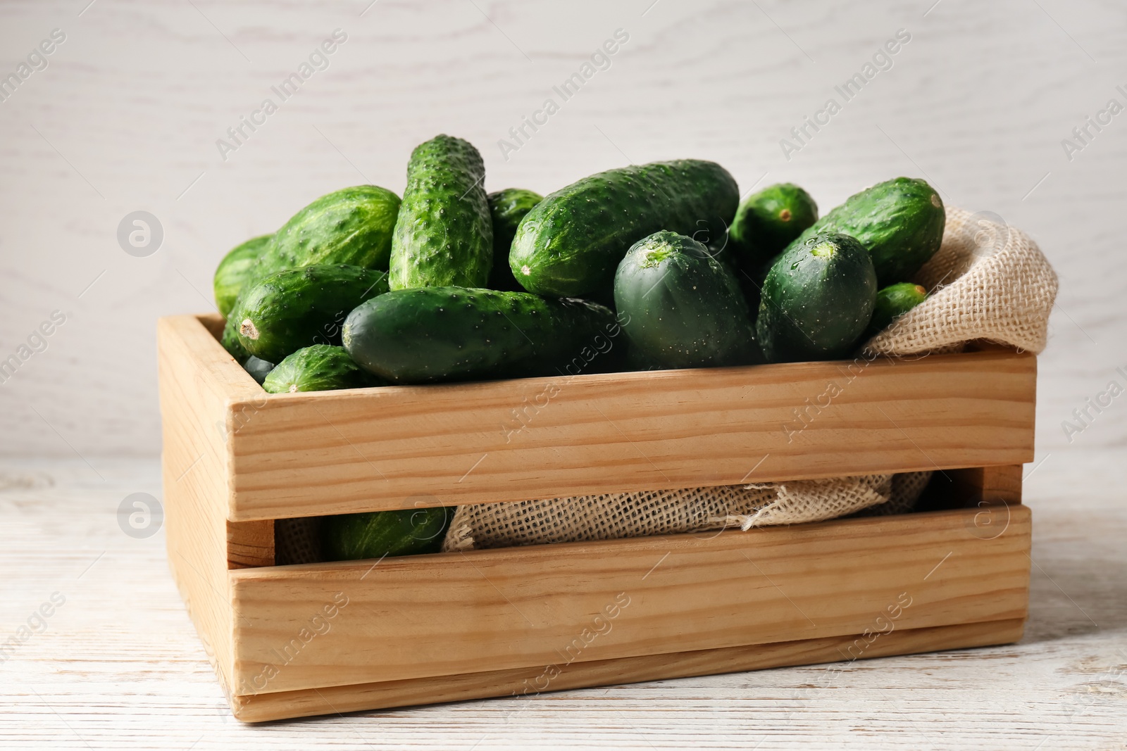 Photo of Crate full of fresh ripe cucumbers on white wooden table