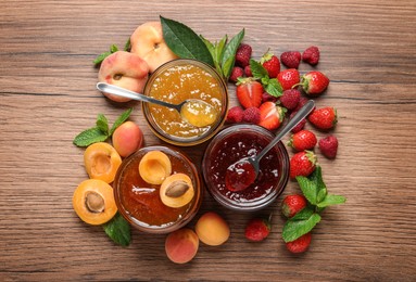 Photo of Jars with different jams and fresh fruits on wooden table, flat lay