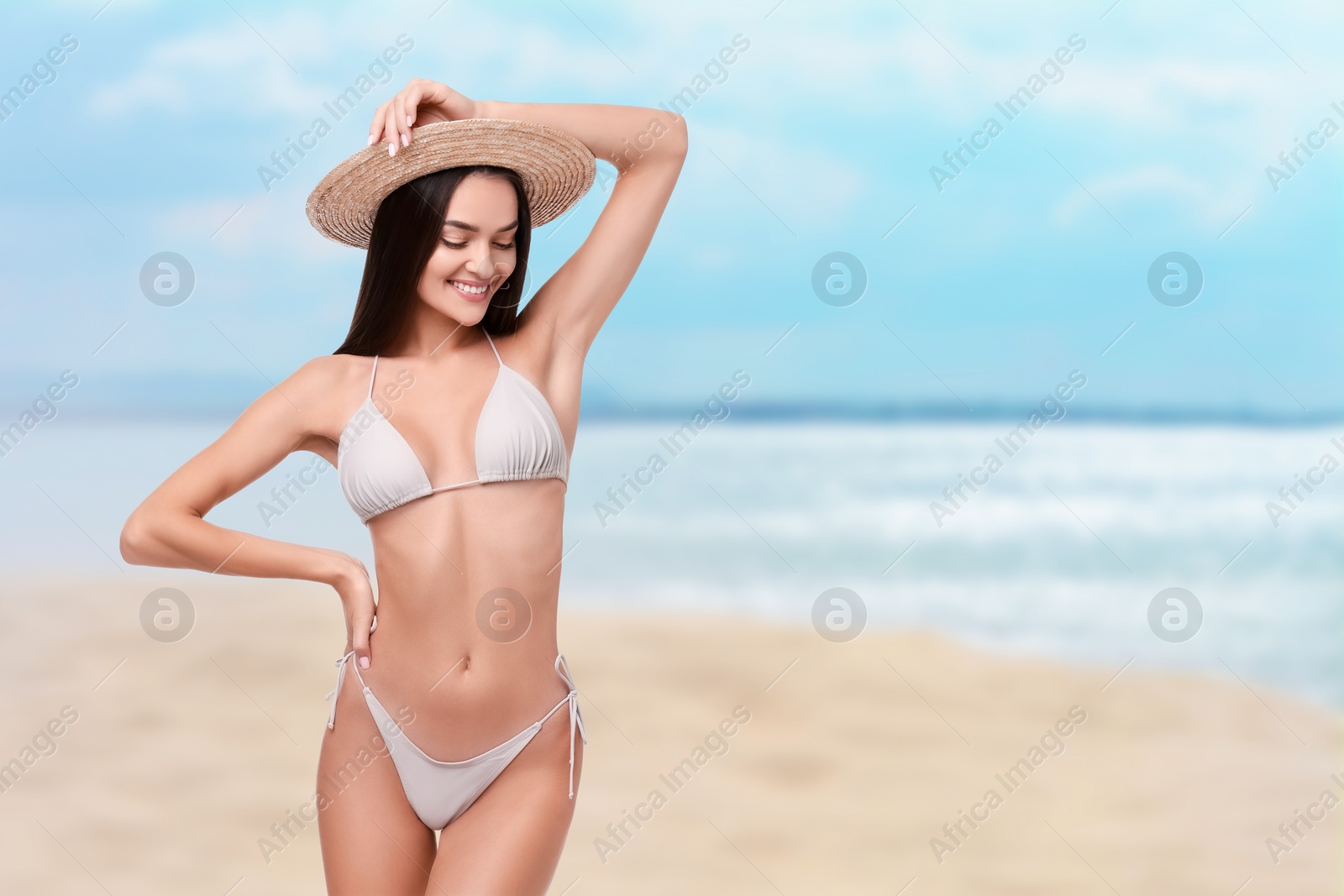 Image of Happy woman in stylish bikini and hat on sandy beach near sea, space for text