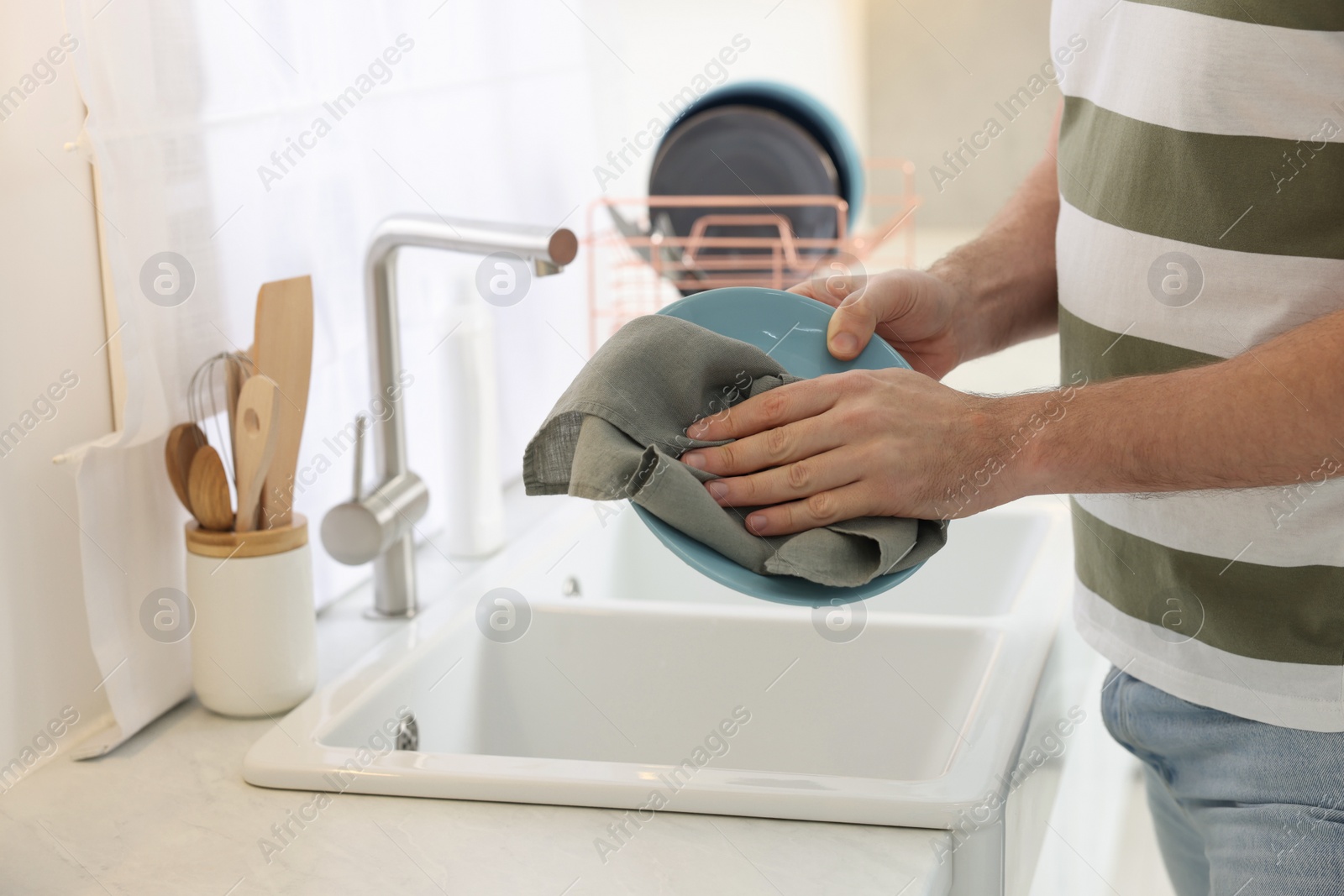 Photo of Man wiping plate with towel above sink in kitchen, closeup