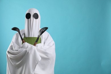 Woman in ghost costume and apron with kitchen set on light blue background, space for text