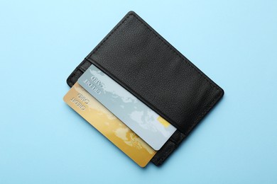 Leather card holder with credit cards on light blue background, top view