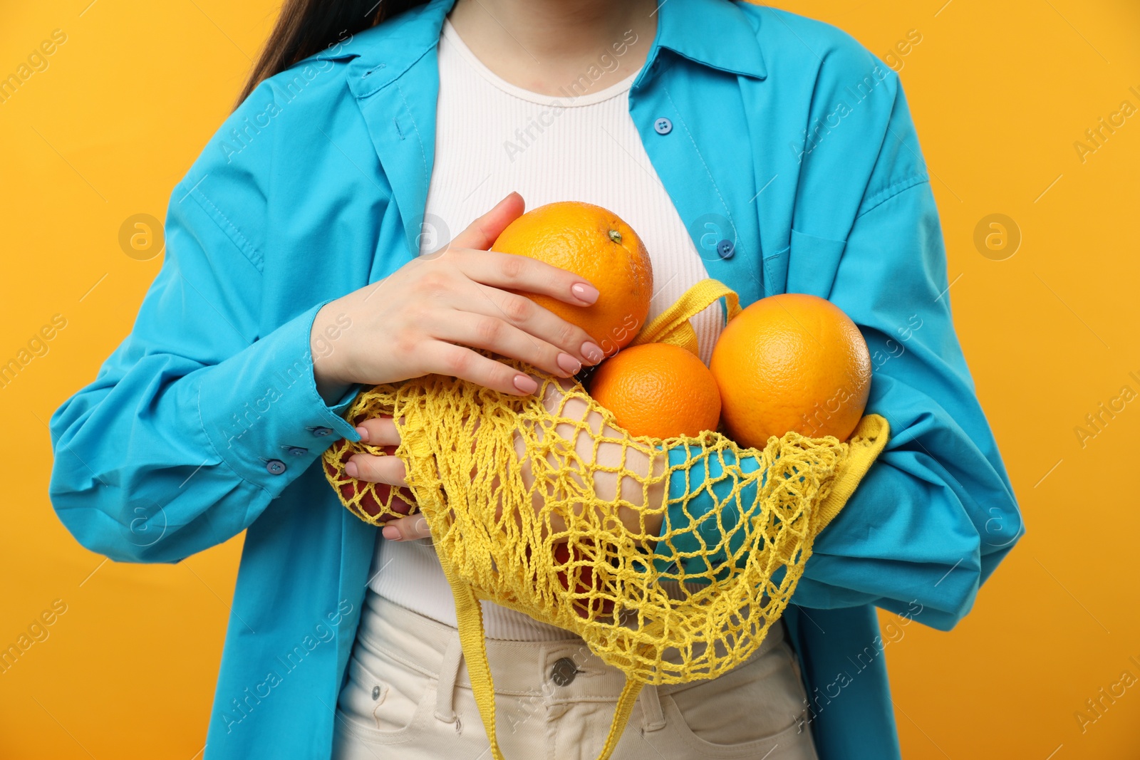 Photo of Woman with string bag of fresh oranges on orange background, closeup