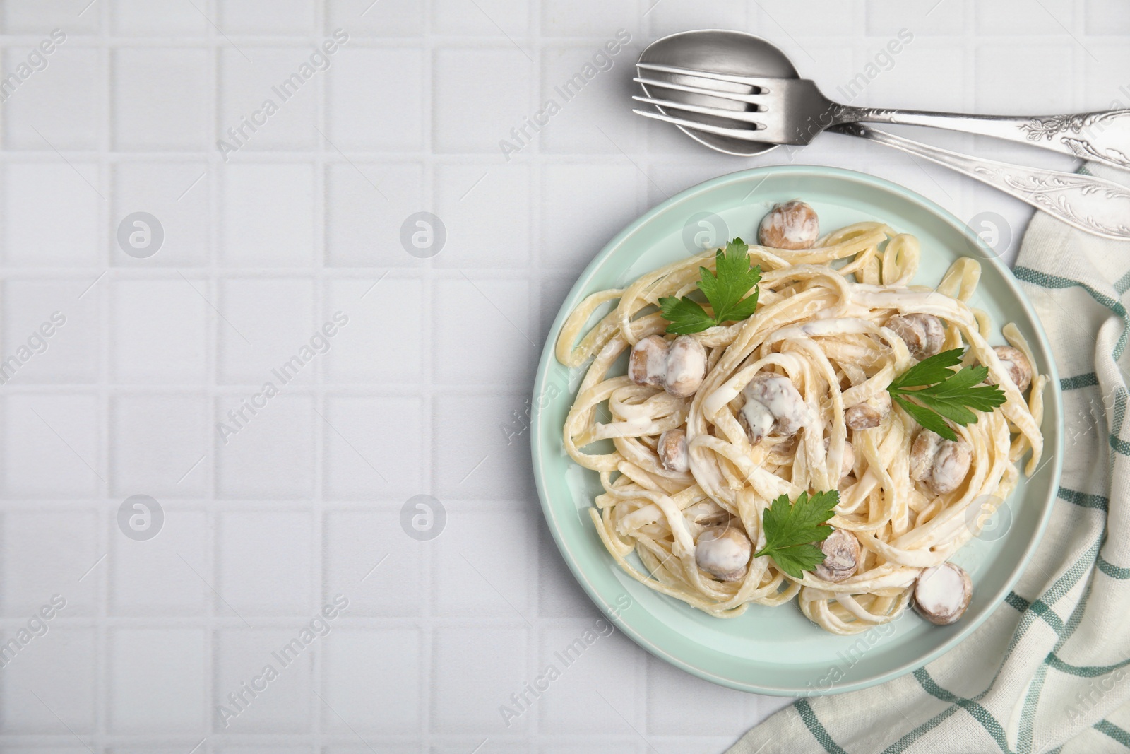 Photo of Delicious pasta with mushrooms served on white tiled table, flat lay. Space for text