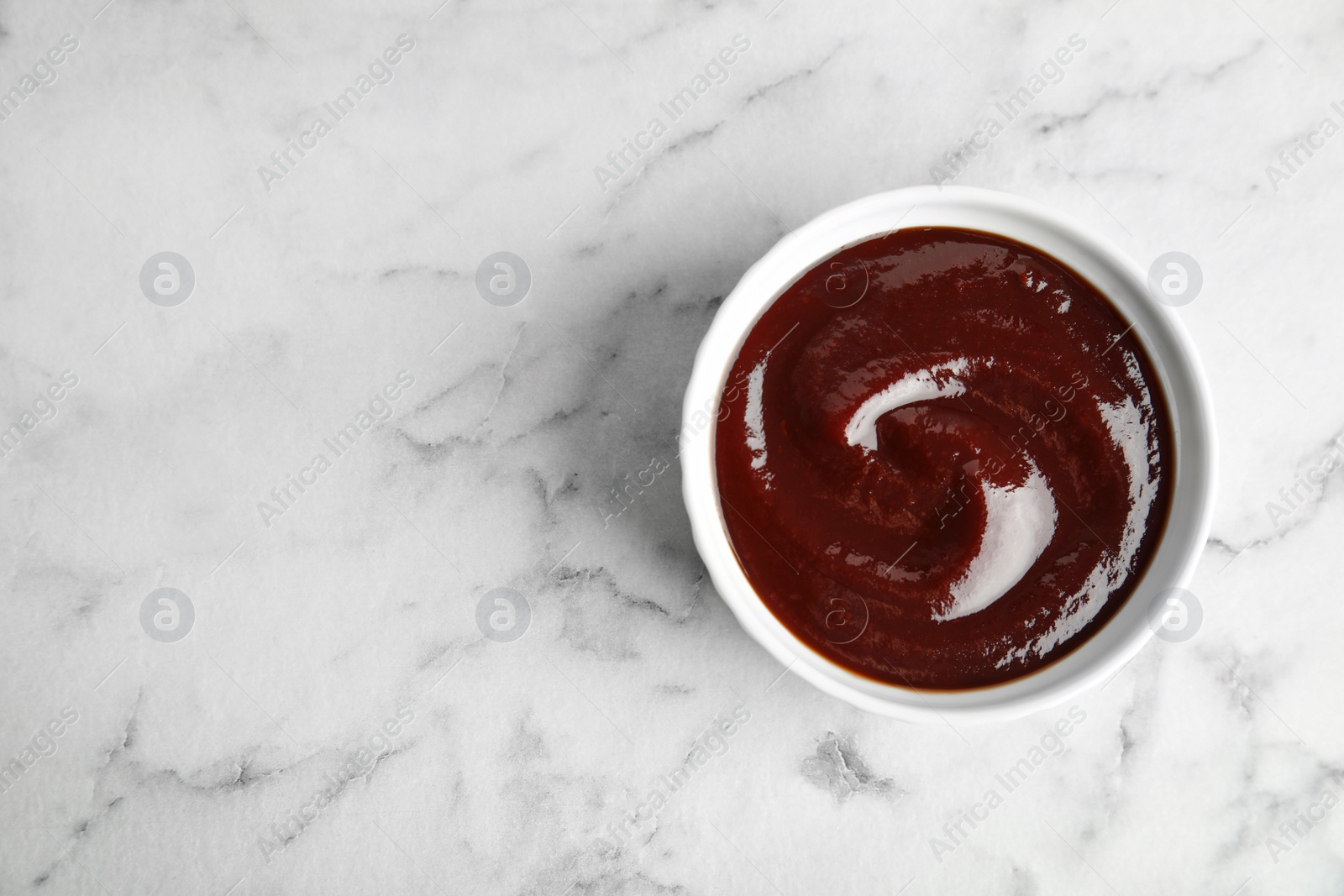 Photo of Barbecue sauce in bowl on marble background, top view. Space for text