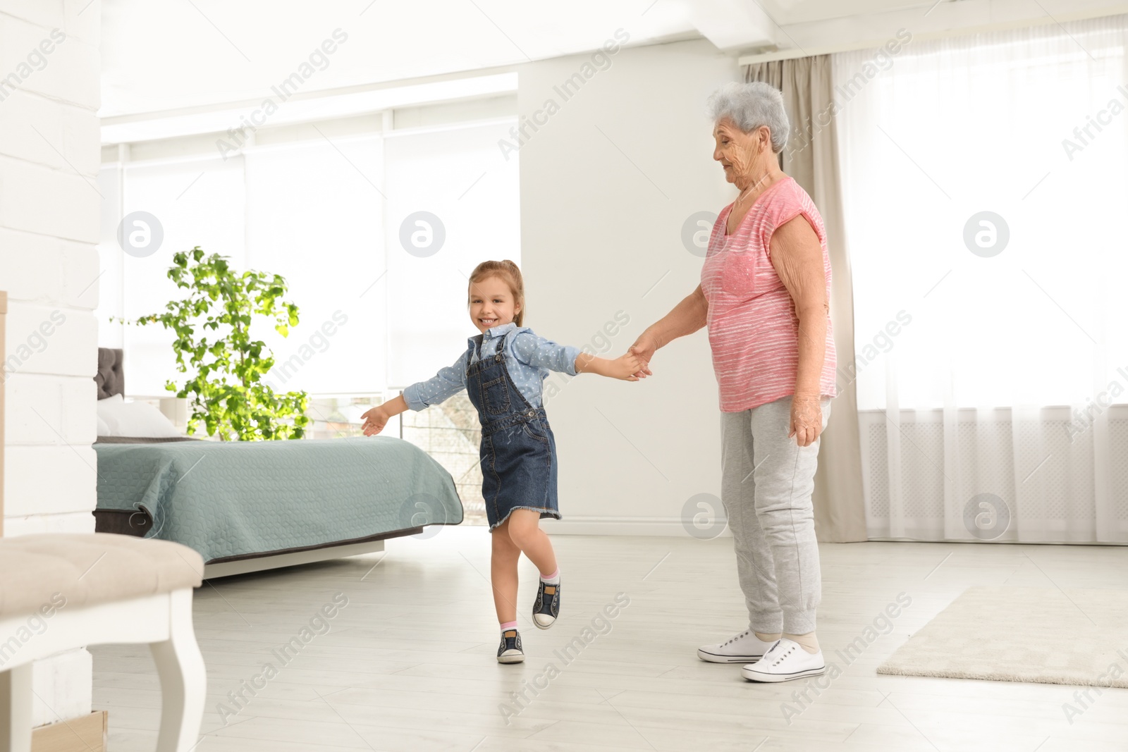 Photo of Cute girl and her grandmother dancing at home