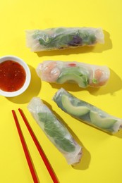 Photo of Delicious spring rolls, sauce and chopsticks on yellow background, flat lay