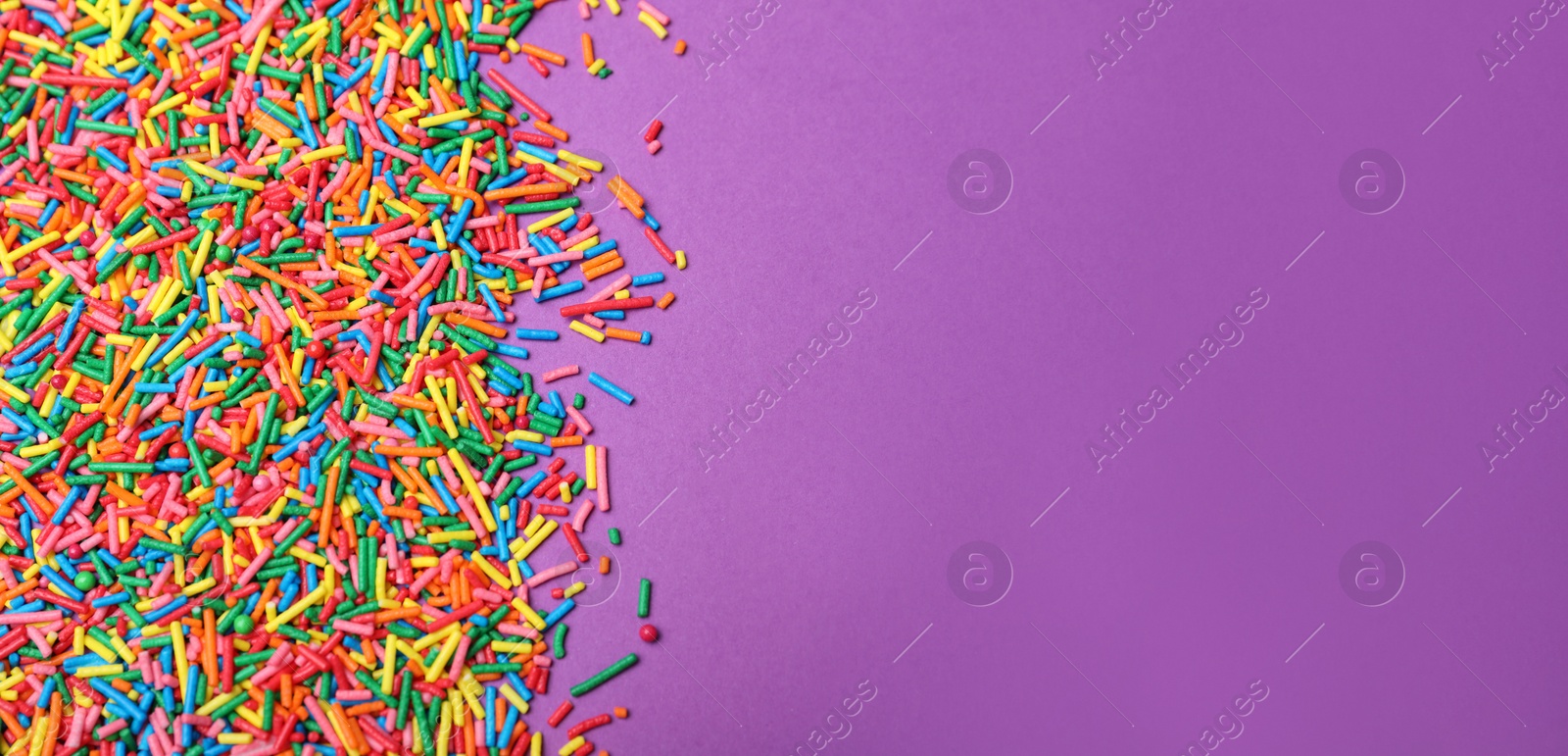 Photo of Colorful sprinkles on purple background, flat lay with space for text. Confectionery decor