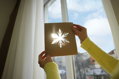 Photo of Woman holding snowflake stencil near window at home, closeup