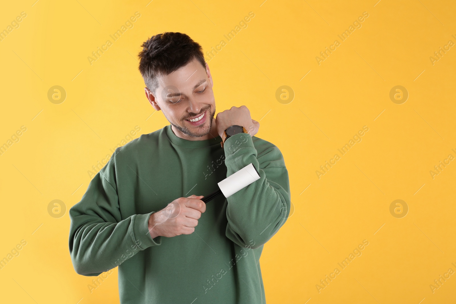 Photo of Man cleaning clothes with lint roller on yellow background. Space for text