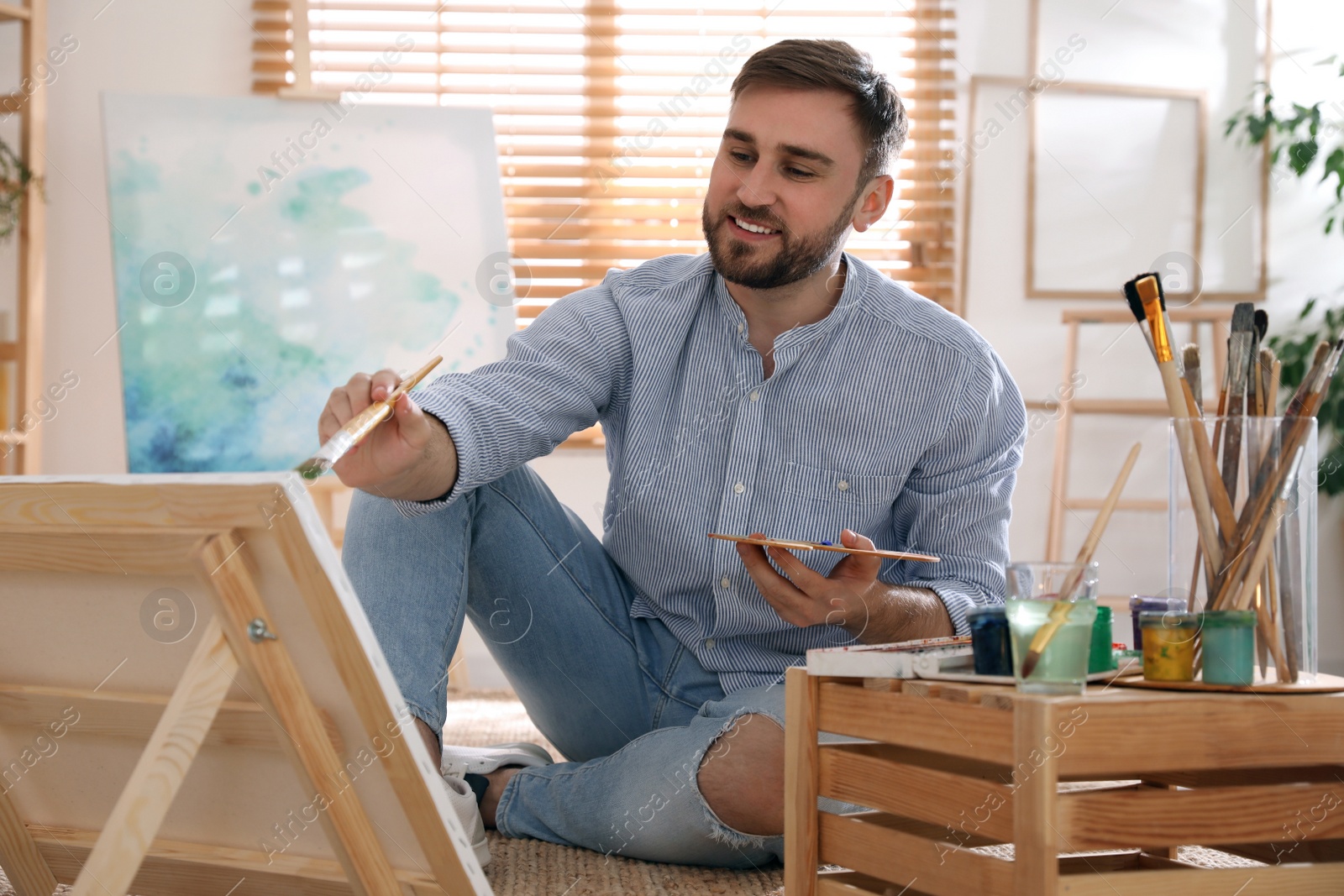 Photo of Young man painting on easel with brush in artist studio