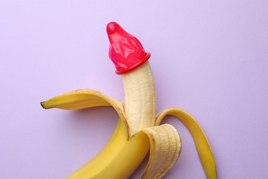 Banana with condom on lilac background, top view. Safe sex concept