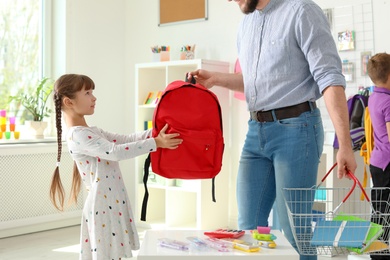 Photo of Little girl choosing school supplies with father in stationery shop