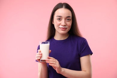 Photo of Cute woman with milk mustache holding glass of tasty dairy drink on pink background