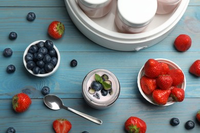 Modern yogurt maker with full jars and different fruits on light blue wooden table, flat lay