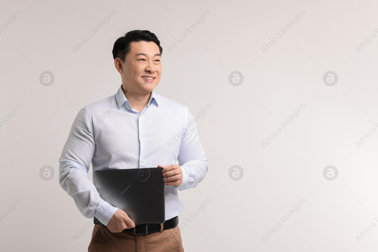 Photo of Portrait of happy man with laptop on light background. Space for text