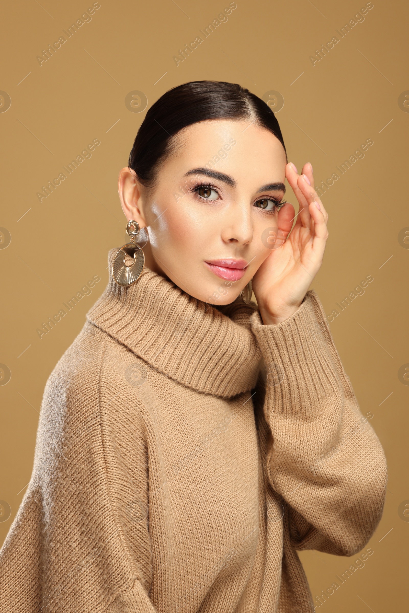 Photo of Beautiful young woman with elegant earrings on light brown background