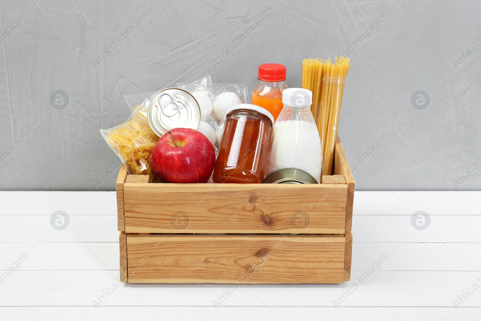 Photo of Humanitarian aid. Different food products for donation in crate on white wooden table