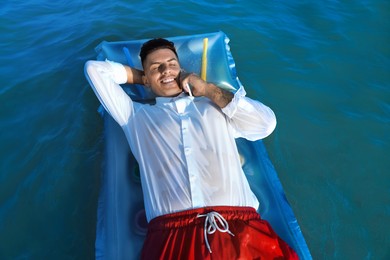 Photo of Happy man talking by mobile phone while floating on mattress in sea. Business trip