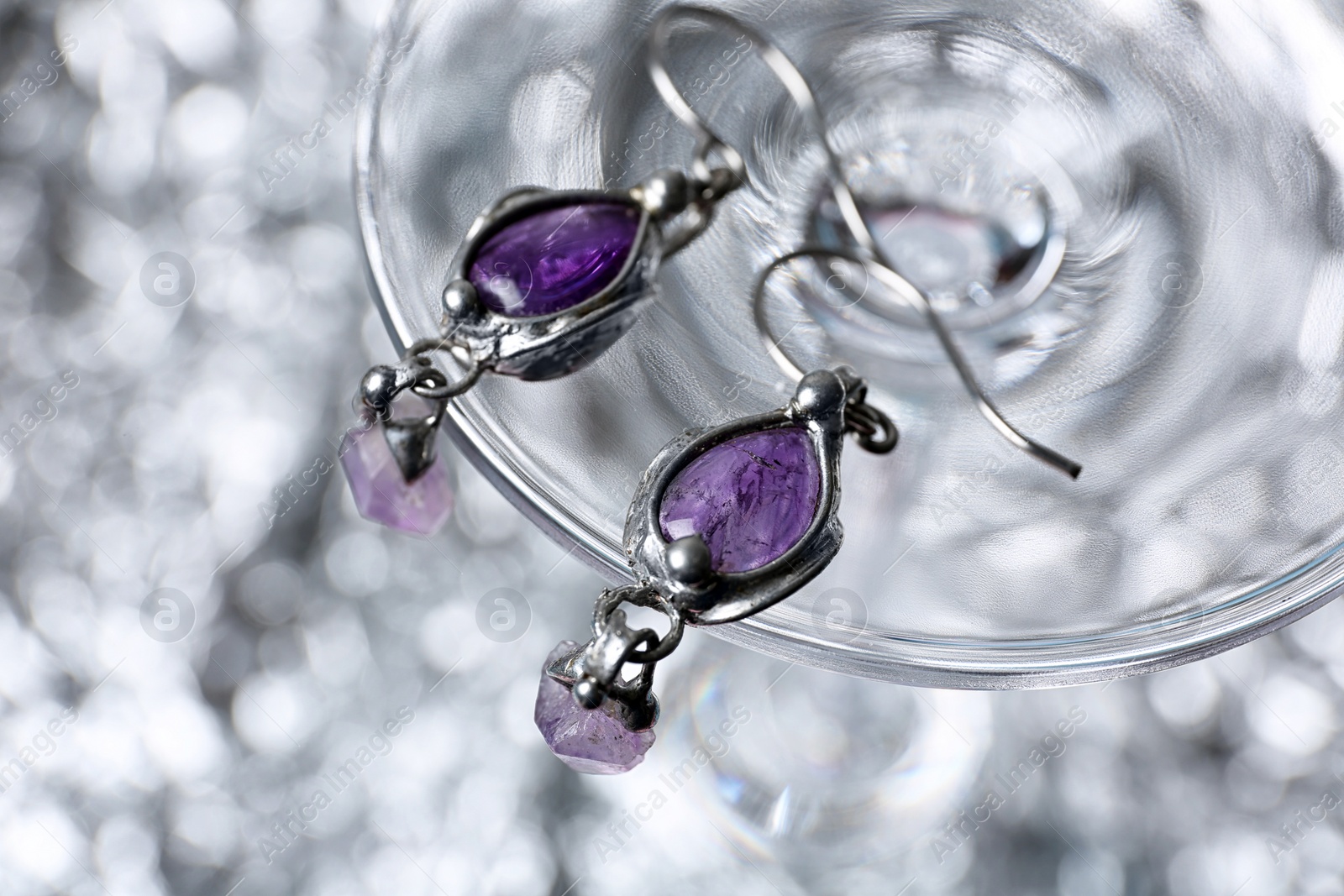Photo of Closeup of beautiful pair of silver earrings with amethyst gemstones on blurred background