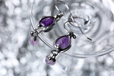 Photo of Closeup of beautiful pair of silver earrings with amethyst gemstones on blurred background