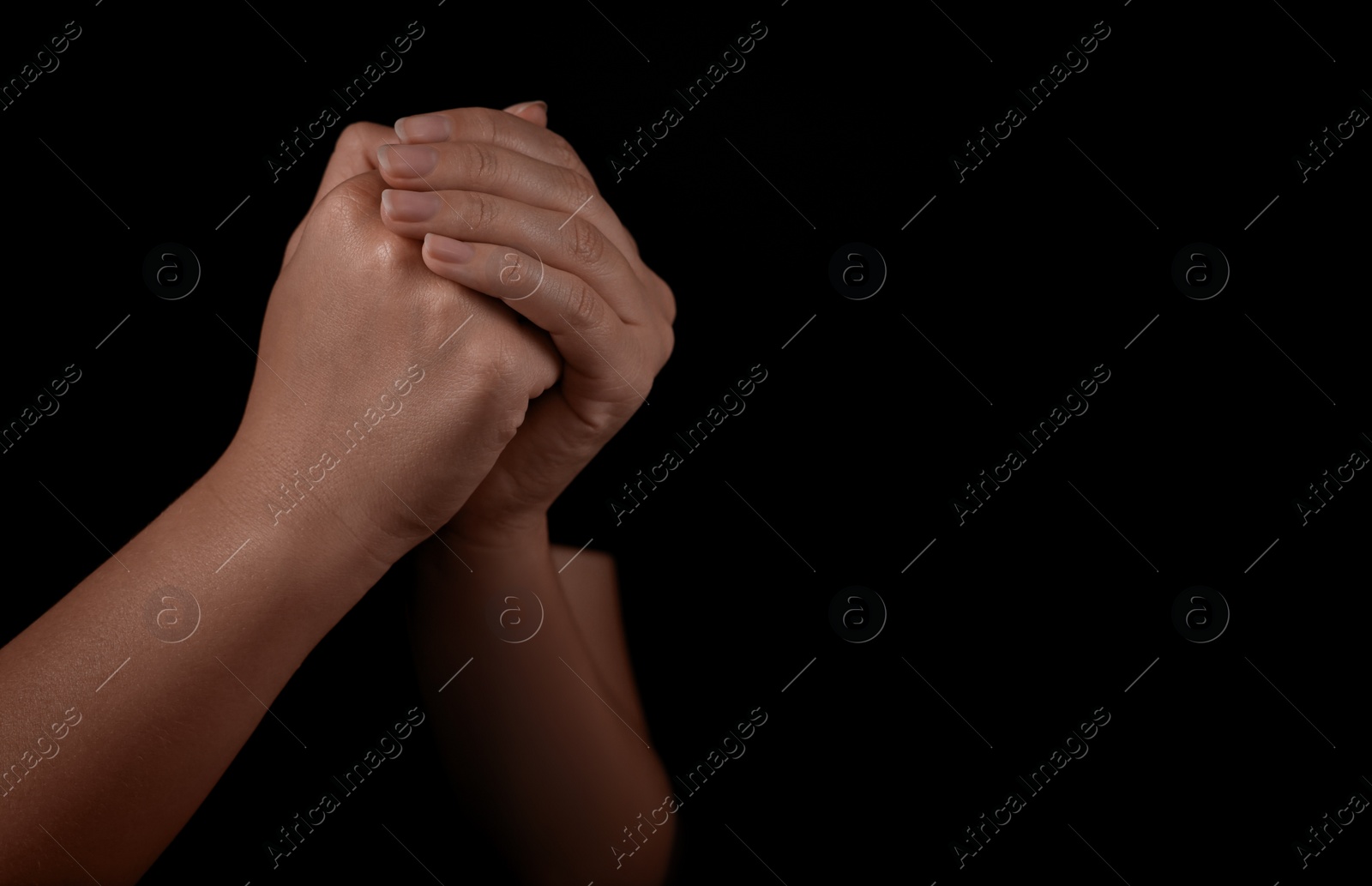 Photo of Woman holding hands clasped while praying against black background, closeup. Space for text