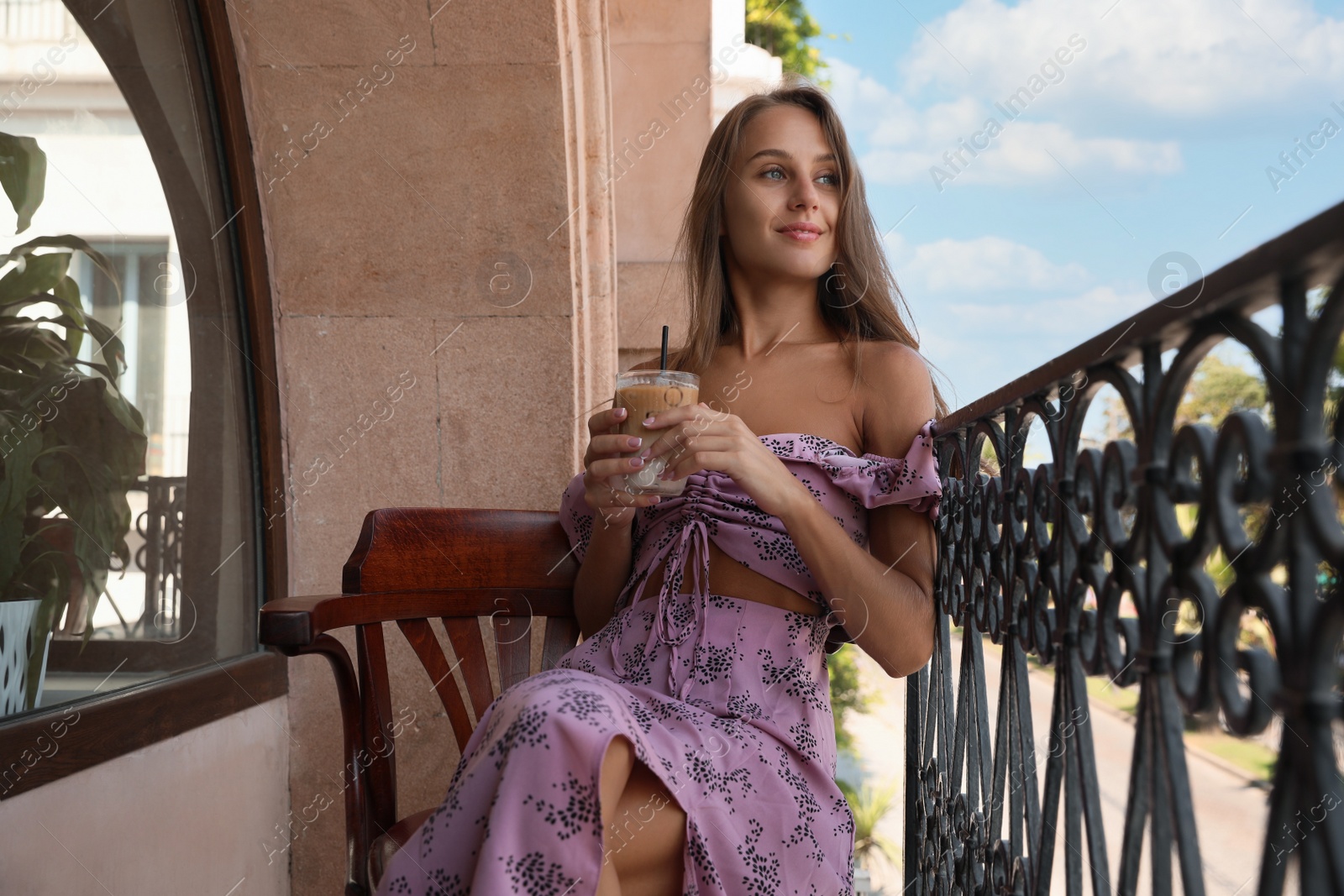 Photo of Young woman with glass of coffee sitting on balcony