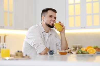 Smiling man drinking juice at breakfast indoors