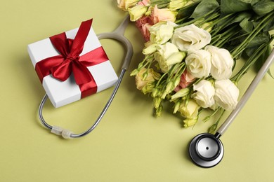 Photo of Stethoscope, gift box and flowers on green background, above view. Happy Doctor's Day