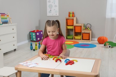 Motor skills development. Girl playing with colorful wooden arcs at white table in kindergarten