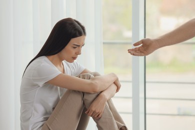 Photo of Man offering hand to depressed woman indoors