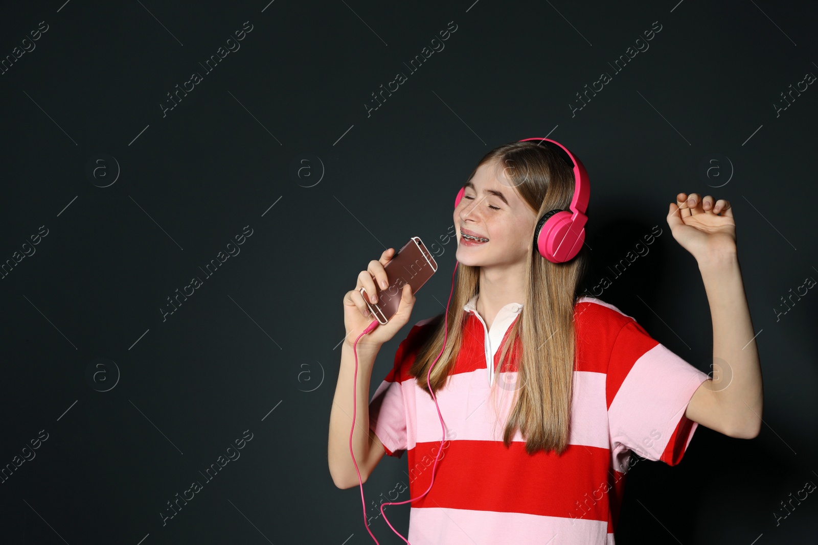 Photo of Teenage girl enjoying music in headphones on black background. Space for text