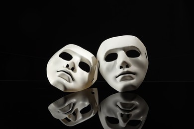 Photo of Plastic face masks on black mirror surface. Theatrical performance