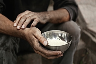 Photo of Poor homeless man with bowl of rice outdoors, closeup