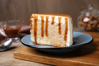 Slice of delicious cake with caramel sauce on wooden table