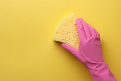 Photo of Cleaner in rubber glove holding new sponge on yellow background, top view. Space for text