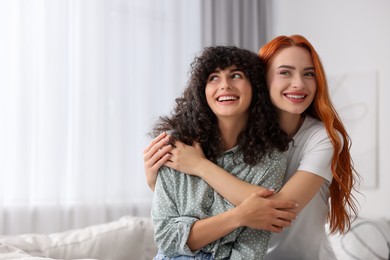 Portrait of happy young friends hugging at home, space for text