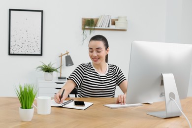 Photo of Home workplace. Happy woman working at wooden desk in room