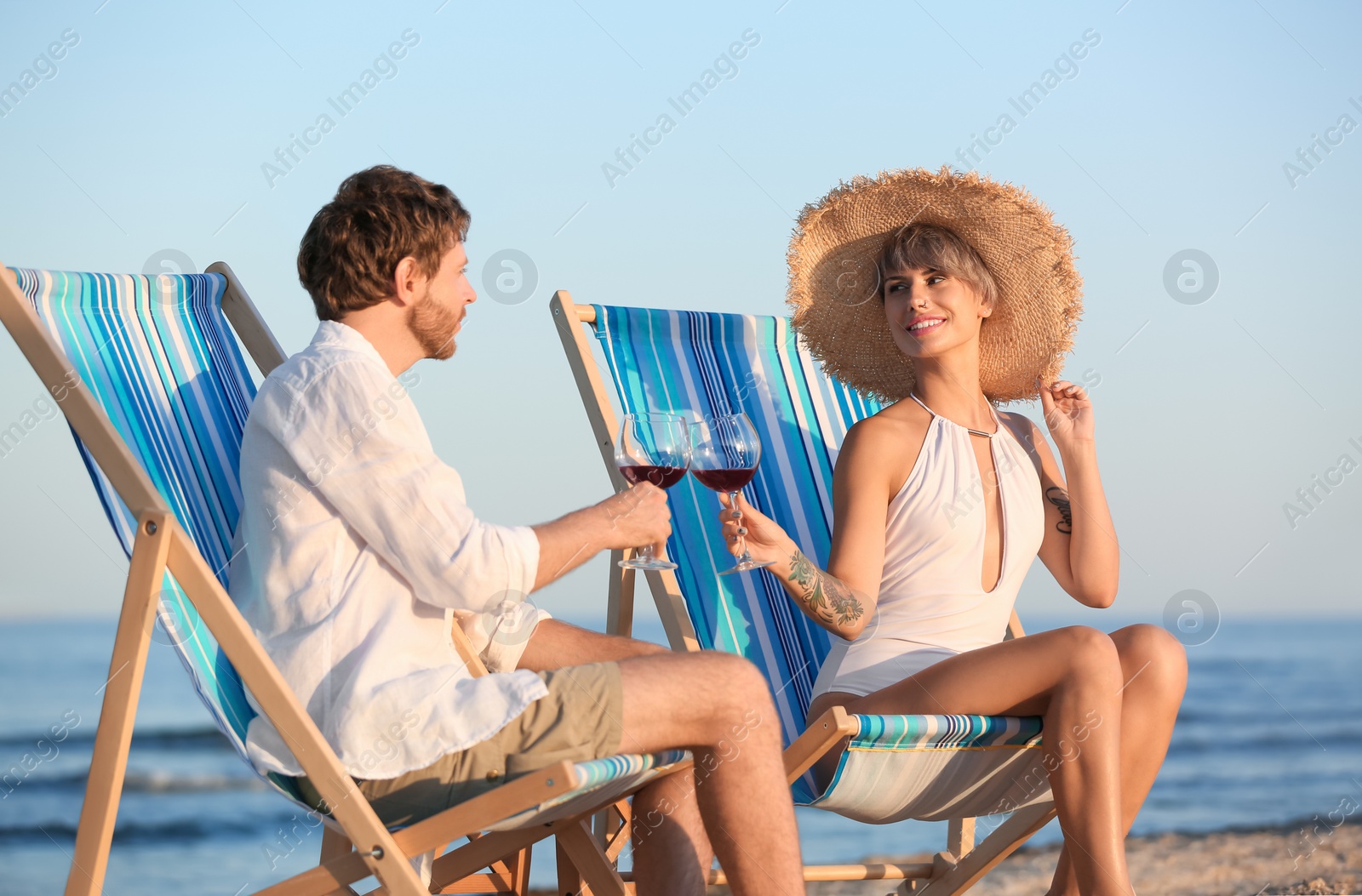 Photo of Young couple with glasses of wine in beach chairs at seacoast