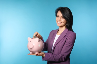 Beautiful businesswoman putting money into piggy bank on color background. Space for text