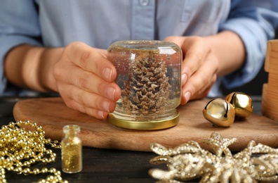 Photo of Woman making snow globe at black wooden table, closeup