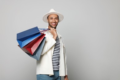 Photo of Happy African American man in hat with shopping bags on light grey background. Space for text
